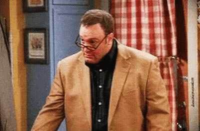 A Man Wearing Glasses And A Tan Suit Is Standing In A Room GIF