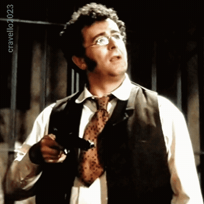 A Man Wearing Glasses And A Tie Is Holding A Gun In Front Of A Sign That Says Cravello40253 GIF