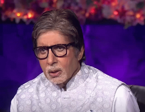 A Man Wearing Glasses And A Vest Is Sitting In Front Of A Purple Background GIF