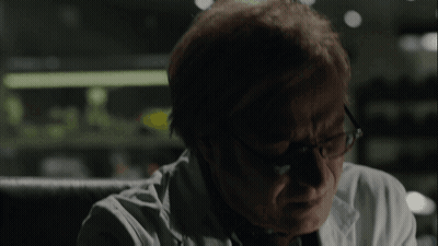 A Man Wearing Glasses And A White Coat Looks Down GIF