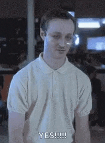 A Man Wearing Glasses And A White Polo Shirt Is Standing In A Room . GIF