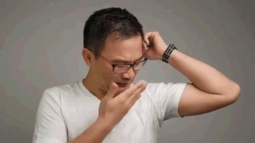 A Man Wearing Glasses And A White Shirt Is Covering His Nose With His Hand . GIF