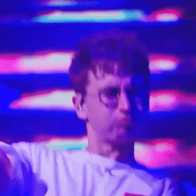 A Man Wearing Glasses And A White Shirt Is Dancing In Front Of A Purple And Pink Background . GIF