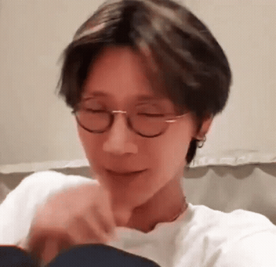 A Man Wearing Glasses And A White Shirt Is Sitting On A Couch . GIF