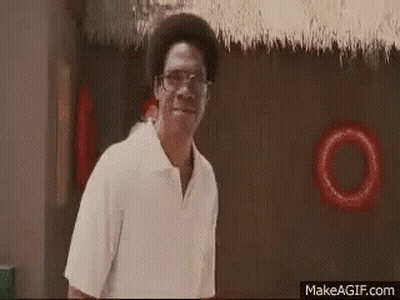 A Man Wearing Glasses And A White Shirt Is Standing In Front Of A Thatched Roof And Smiling . GIF