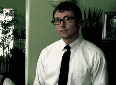 A Man Wearing Glasses And A White Shirt Stands In Front Of A Picture GIF