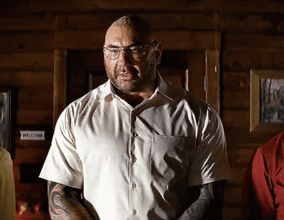A Man Wearing Glasses And A White Shirt Stands In Front Of A Sign That Says Welcome GIF