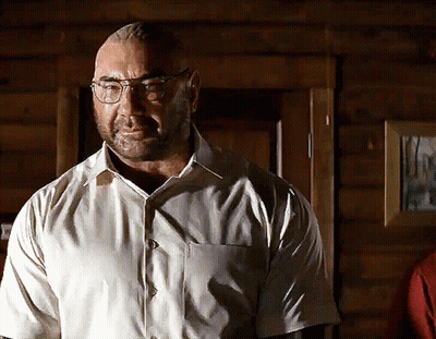 A Man Wearing Glasses And A White Shirt Stands In Front Of A Wooden Door GIF