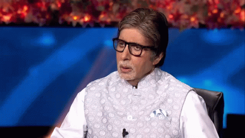 A Man Wearing Glasses And A White Vest Is Sitting In Front Of A Microphone . GIF