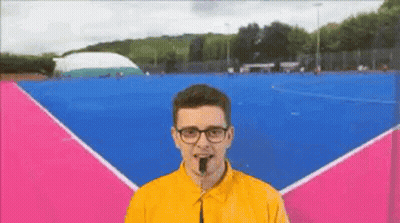 A Man Wearing Glasses And A Yellow Shirt Is Standing In Front Of A Blue And Pink Court GIF