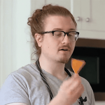 A Man Wearing Glasses And An Apron Is Eating A Chip GIF