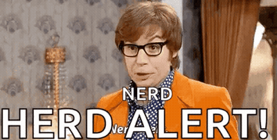 A Man Wearing Glasses And An Orange Jacket Is Standing In Front Of A Wall That Says Herd Alert . GIF
