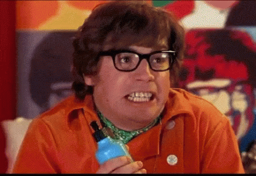 A Man Wearing Glasses And An Orange Shirt Is Holding A Blue Bottle And Making A Funny Face . GIF
