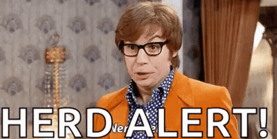 A Man Wearing Glasses And An Orange Suit Is Standing In A Room With The Words Herd Alert Written On The Wall . GIF