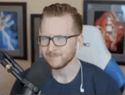A Man Wearing Glasses And Ear Buds Is Sitting In Front Of A Microphone In A Room . GIF