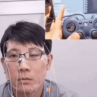 A Man Wearing Glasses And Earbuds Is Holding A Logitech Controller In Front Of His Face GIF