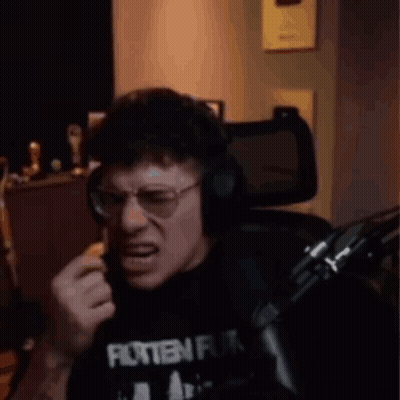 A Man Wearing Glasses And Headphones Is Sitting In Front Of A Microphone And Making A Funny Face . GIF