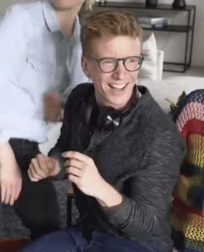 A Man Wearing Glasses And Headphones Is Sitting On A Couch And Smiling . GIF