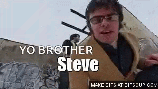 A Man Wearing Glasses And Headphones Is Standing In Front Of A Wall With Graffiti On It . GIF