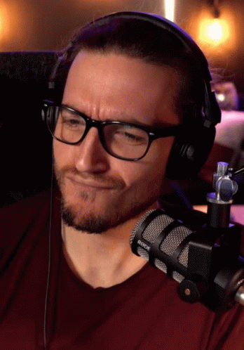 A Man Wearing Glasses And Headphones With A Rode Microphone In Front Of Him GIF