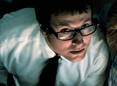 A Man Wearing Glasses And Suspenders Is Looking At Something GIF