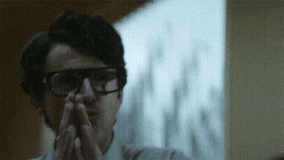 A Man Wearing Glasses Has His Hands Folded In Front Of Him GIF