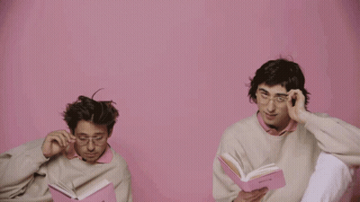 A Man Wearing Glasses Holds A Pink Book That Says ' Poetry ' On It GIF