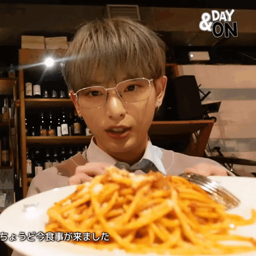 A Man Wearing Glasses Holds A Plate Of Spaghetti In Front Of A Sign That Says " Day & On " GIF