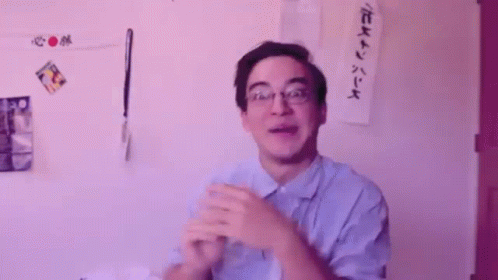 A Man Wearing Glasses Is Clapping His Hands In Front Of A Wall That Says Oooooooh GIF