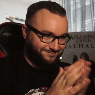 A Man Wearing Glasses Is Clapping In Front Of A Assassin Creed Valhal Poster GIF