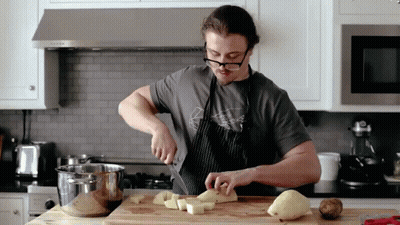 A Man Wearing Glasses Is Cutting Potatoes On A Wooden Cutting Board GIF