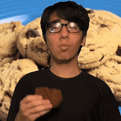 A Man Wearing Glasses Is Eating A Cookie In Front Of A Pile Of Cookies GIF
