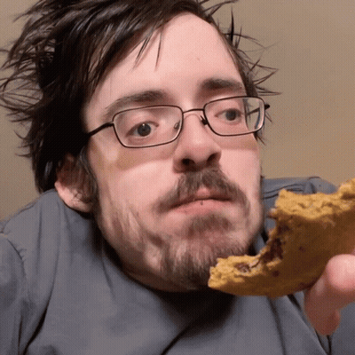 A Man Wearing Glasses Is Eating A Cookie With A Bite Taken Out Of It GIF