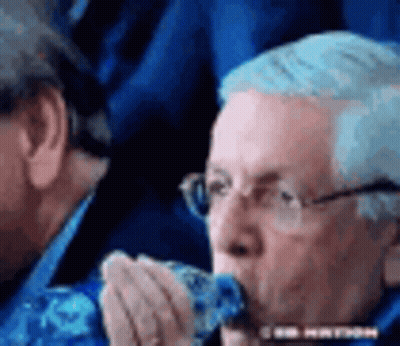 A Man Wearing Glasses Is Eating A Piece Of Food While Sitting In A Stadium . GIF