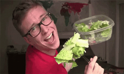 A Man Wearing Glasses Is Eating Lettuce From A Plastic Container With Chopsticks . GIF
