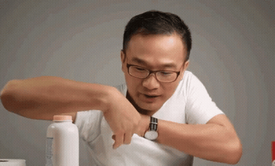 A Man Wearing Glasses Is Holding A Bottle Of Baby Powder In His Pocket GIF