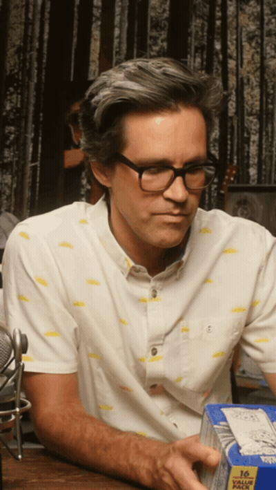 A Man Wearing Glasses Is Holding A Box Of 16 Value Pack GIF