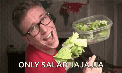 A Man Wearing Glasses Is Holding A Container Of Lettuce And A Fork . GIF