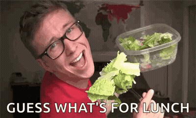 A Man Wearing Glasses Is Holding A Container Of Lettuce And A Piece Of Lettuce On A Fork . GIF