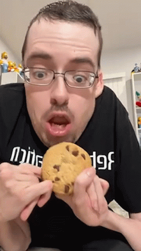 A Man Wearing Glasses Is Holding A Cookie In His Hands GIF