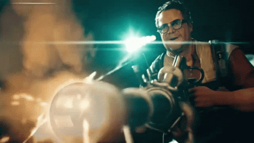 A Man Wearing Glasses Is Holding A Gun In A Dark Room .. GIF