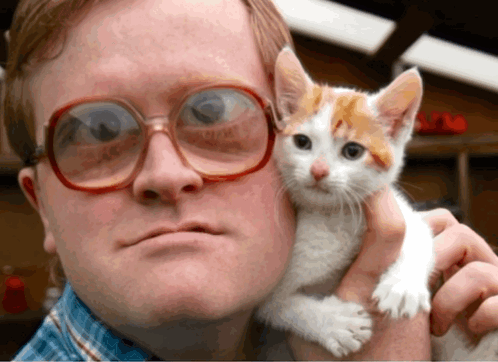 A Man Wearing Glasses Is Holding A Kitten In His Arms GIF