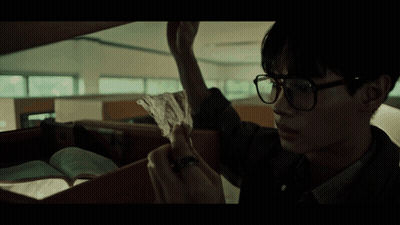 A Man Wearing Glasses Is Holding Another Man 'S Hand In A Dark Room GIF