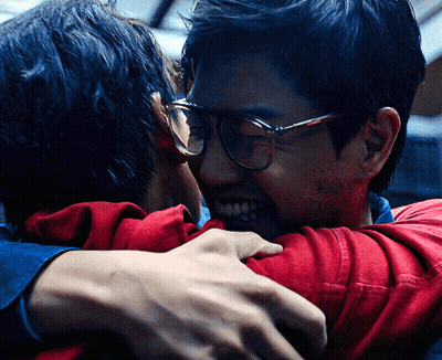 A Man Wearing Glasses Is Hugging Another Man Wearing A Red Shirt GIF