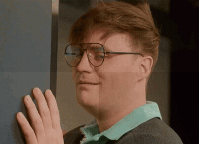 A Man Wearing Glasses Is Leaning Against A Wall With His Hand GIF