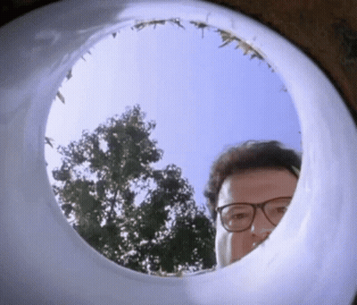 A Man Wearing Glasses Is Looking Through A Hole In A Toilet Bowl . GIF