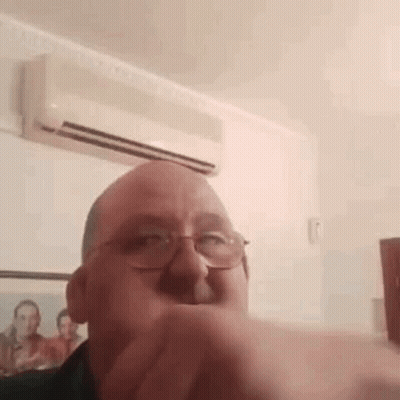 A Man Wearing Glasses Is Making A Funny Face In Front Of An Air Conditioner In A Room . GIF