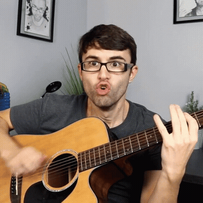 A Man Wearing Glasses Is Playing A Guitar GIF