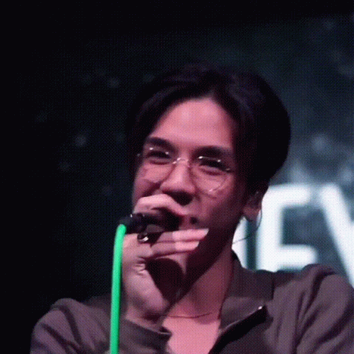 A Man Wearing Glasses Is Singing Into A Microphone On Stage . GIF