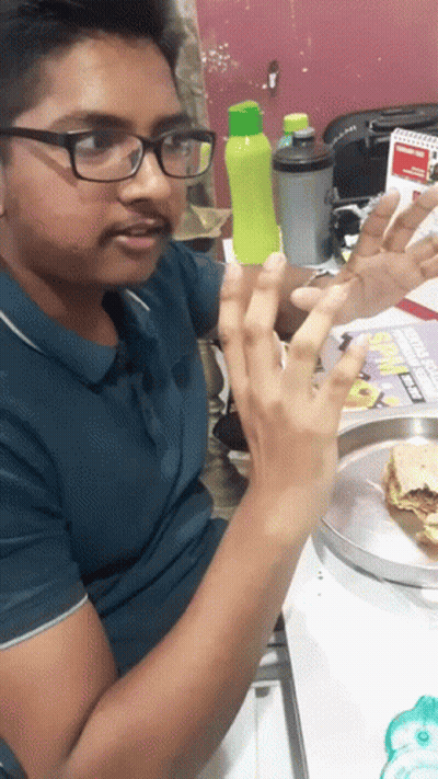 A Man Wearing Glasses Is Sitting At A Table With A Plate Of Food And A Sign That Says Subway GIF